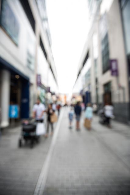 Blurred image of people walking on a busy city street on a sunny day. Ideal for concepts of urban lifestyle, bustling city life, pedestrian traffic, and shopping districts. Useful for backgrounds, presentations on urban planning, or themes involving human activity in public spaces.