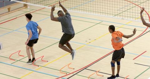 Diverse male athletes jumping agility hurdles while training volleyball footwork in gym