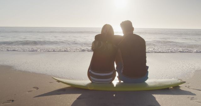 Happy diverse couple sitting on surfboard and embracing on beach. Lifestyle, realxation, nature, free time and vacation.
