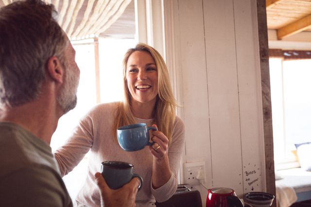 This image depicts a Caucasian couple enjoying a relaxed morning at home, smiling and having coffee together. Ideal for use in lifestyle blogs, advertisements promoting home comfort, coffee brands, or articles about relationships and bonding.