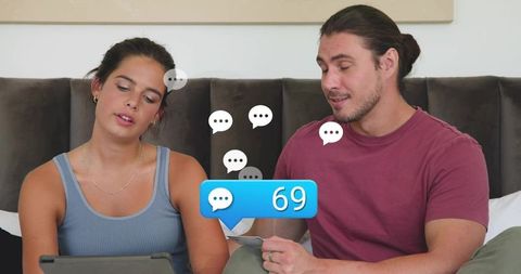 Young couple browsing tablet in cozy bedroom, reacting to 69 message notification