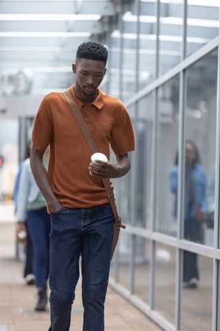 African man walking through glass walkway holding coffee cup and crossbody bag
