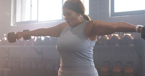 African american woman performing lateral raises with dumbbells in gym strength training