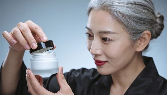 Mature woman inspecting luxury facial cream jar preparing skincare ritual