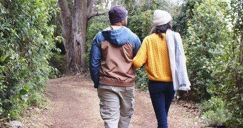 Couple walking arm-in-arm on forest trail wearing knit beanies during autumn stroll