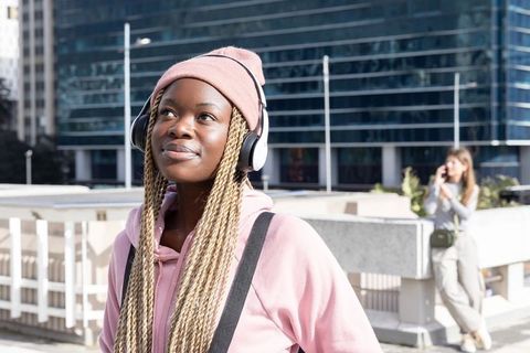 Young African American Woman Wearing Headphones and Pink Hoodie Enjoying Downtown Walk