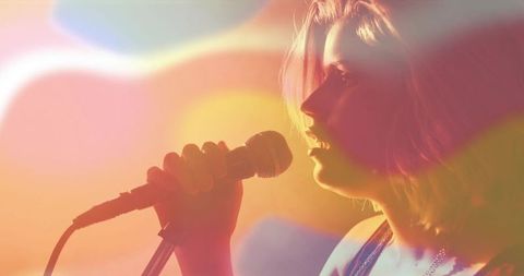 Teen singer performing with wired microphone under warm backlight and colorful lens flares