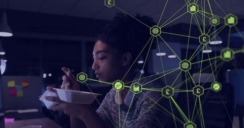 Working late eating takeout at desk while analyzing connected finance data network overlay