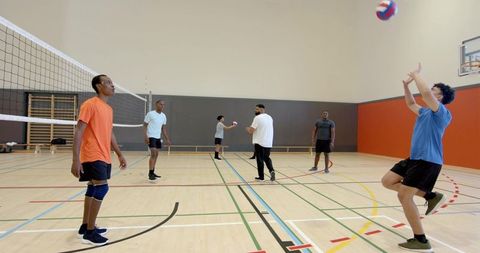 Multiethnic male team practicing indoor volleyball with coach in gymnasium