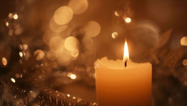 Glowing pillar candle emitting warm amber glow with melted wax rim and silver tinsel