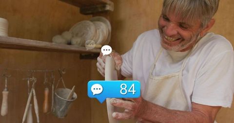 Senior male potter trimming ceramic bowl in warm workshop with social media comment bubble
