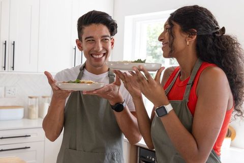 African american couple presenting homemade dishes and smiling in bright modern kitchen