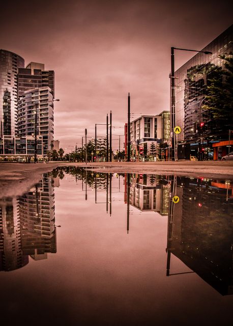 Reflection of city skylines and modern buildings in wet street at dusk, creating a stunning mirror effect. Ideal for use in urban planning presentations, architectural magazines, and travel blogs to evoke a modern city atmosphere.