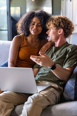 Young couple relaxing on sofa sharing laptop, casual home browsing and planning together