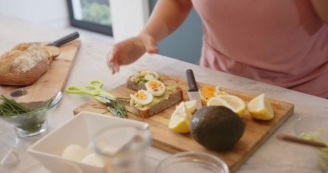 Preparing avocado egg toast on rustic sourdough with herbs, lemon and soft-boiled eggs