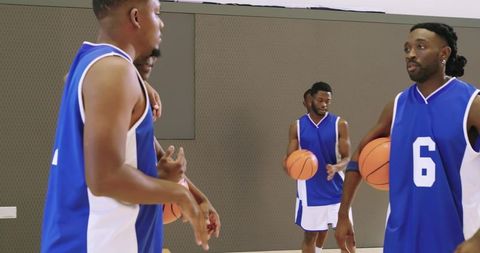 Basketball teammates practicing in indoor court with player 6 holding ball at hip, focused
