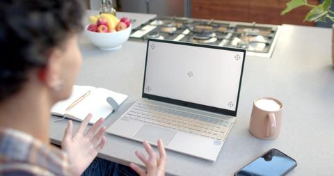 Man gesturing at laptop on kitchen counter working remotely with coffee notebook