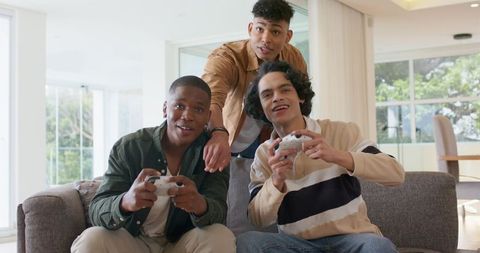 Diverse friends playing console games on couch, laughing and competing in living room