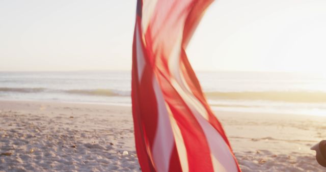 Close up of hands of Caucasian man enjoying time at the beach at sundown, holding and waving US flag , with sunset sky and sea in the background, in slow motion. Summer tropical beach vacation.