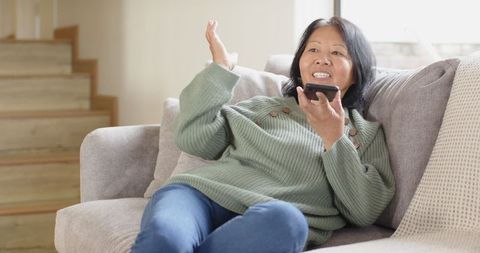 Senior Asian Woman Relaxing at Home Speaking into Smartphone