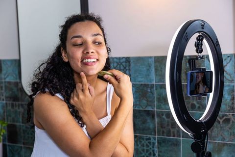 African woman demonstrating facial massage while recording beauty vlog with ring light