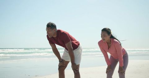 Couple Catching Breath After Beach Workout Wearing Fitness Tracker and Athletic Gear