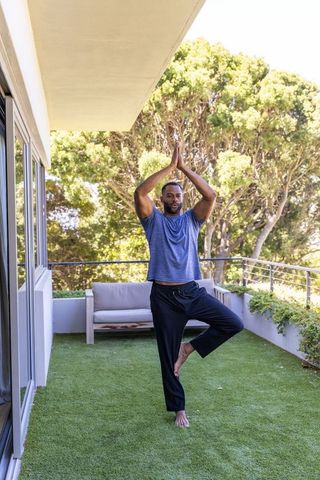 Mature african american man practicing tree pose on balcony for wellness and balance