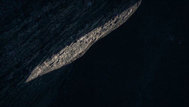 Sunlit Narrow Ledge Cutting Diagonal Through Dark Cliff Face with Rugged Rock Texture