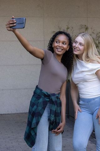 Multiracial friends taking selfie in urban courtyard, natural smiles, casual street style