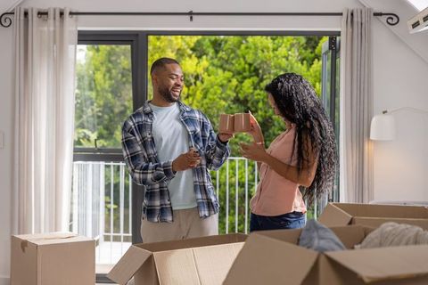 Young african american couple unpacking new home, toasting with mugs on sunny balcony