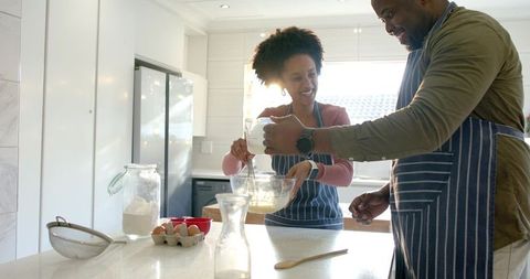 Couple whisking batter together in bright sunlit modern kitchen, teamwork, home cooking joy