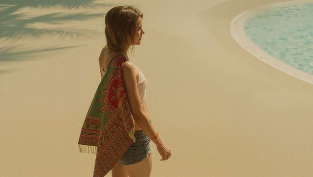 Walking woman wearing tank top and denim shorts by turquoise pool, patterned shawl draped