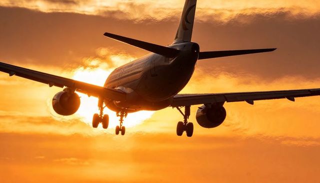 Commercial jetliner descending into golden sunset with landing gear down and backlit silhouette