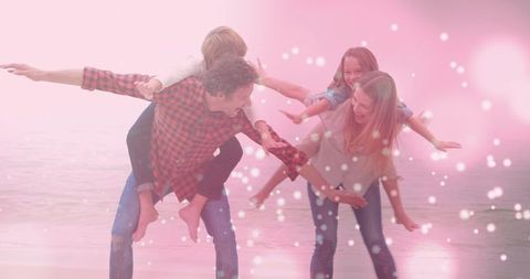 Parents giving piggyback rides on beach shoreline with pastel bokeh and wet sand glow