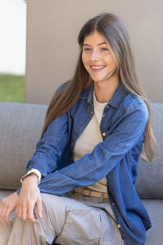 Young woman sitting on outdoor sofa smiling in denim shirt and cargo pants showing wristwatch