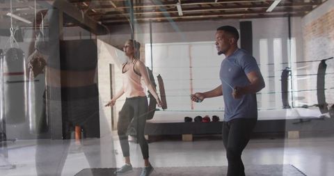 Partners skipping rope for cardio training in industrial boxing gym with ring and weights