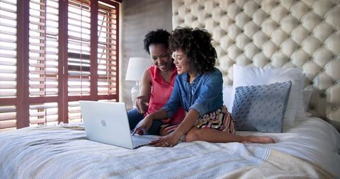 Diverse Female Couple Relaxing with Laptop in Cozy Bedroom