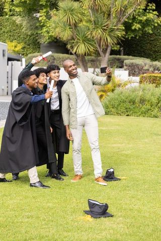 Smiling graduates taking selfie with african american father on graduation day