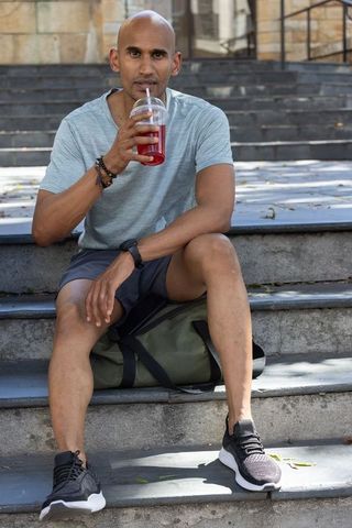 African american man sitting on urban steps sipping red drink after outdoor workout
