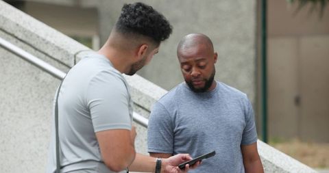 Diverse colleagues collaborating outdoors on smartphone at concrete stairwell