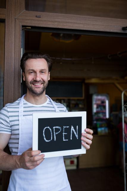 Portrait of smiling owner holding a open sign at bakery shop entrance