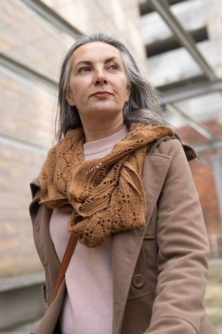 Mature woman looking upward left in urban courtyard wearing tan coat and knitted scarf