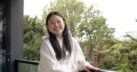 Asian woman relaxing on balcony in white sweatshirt smiling urban lifestyle portrait