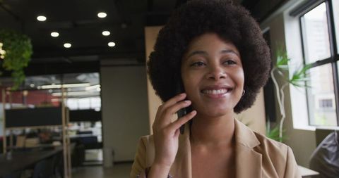 Businesswoman smiling while talking on smartphone in modern office space