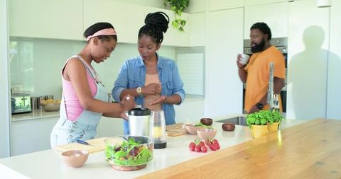 African women preparing healthy salad with blender and fresh herbs at kitchen island