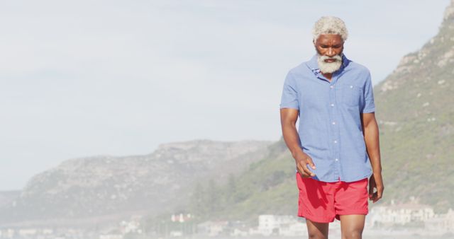 Senior african american man walking alone on sunny beach. healthy and active time beach holiday.
