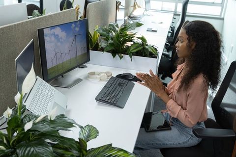 African-american woman working at modern office desk viewing wind turbines on monitor