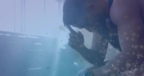 Tired athletic man sitting on bench holding head beneath high window light in locker room