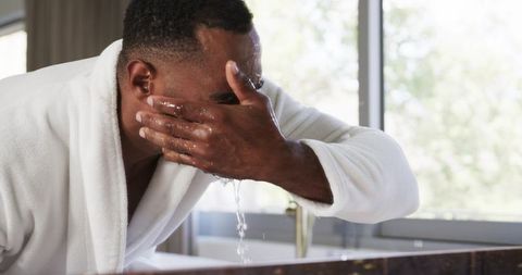 Mature man splashing face at marble vanity during natural light morning grooming routine