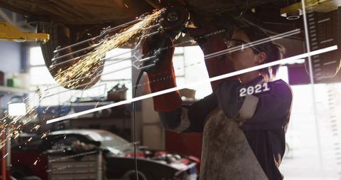 Female Mechanic Grinding Undercarriage Sparks in Auto Repair Garage Workshop with PPE Safety